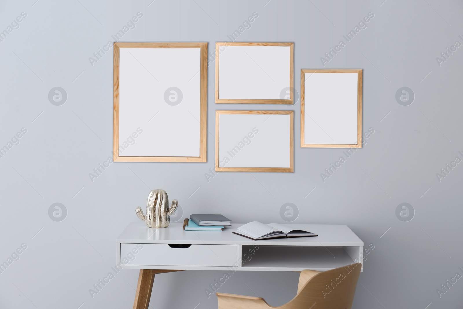 Image of Table and chair near light grey wall with empty posters. Mockup for design