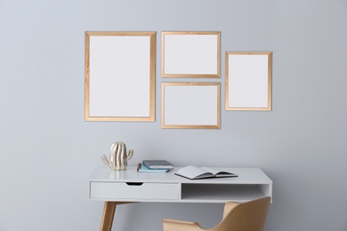 Image of Table and chair near light grey wall with empty posters. Mockup for design