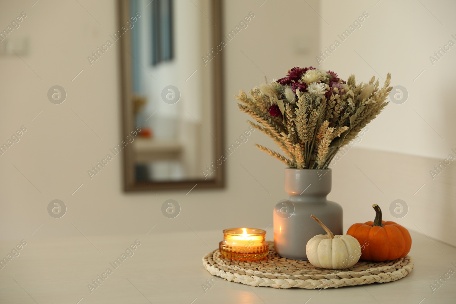 Photo of Beautiful bouquet of dry flowers, small pumpkins and candle on white table indoors, space for text