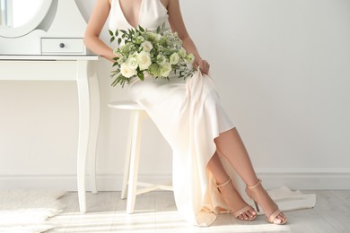 Photo of Young bride wearing wedding dress with beautiful bouquet in room, closeup