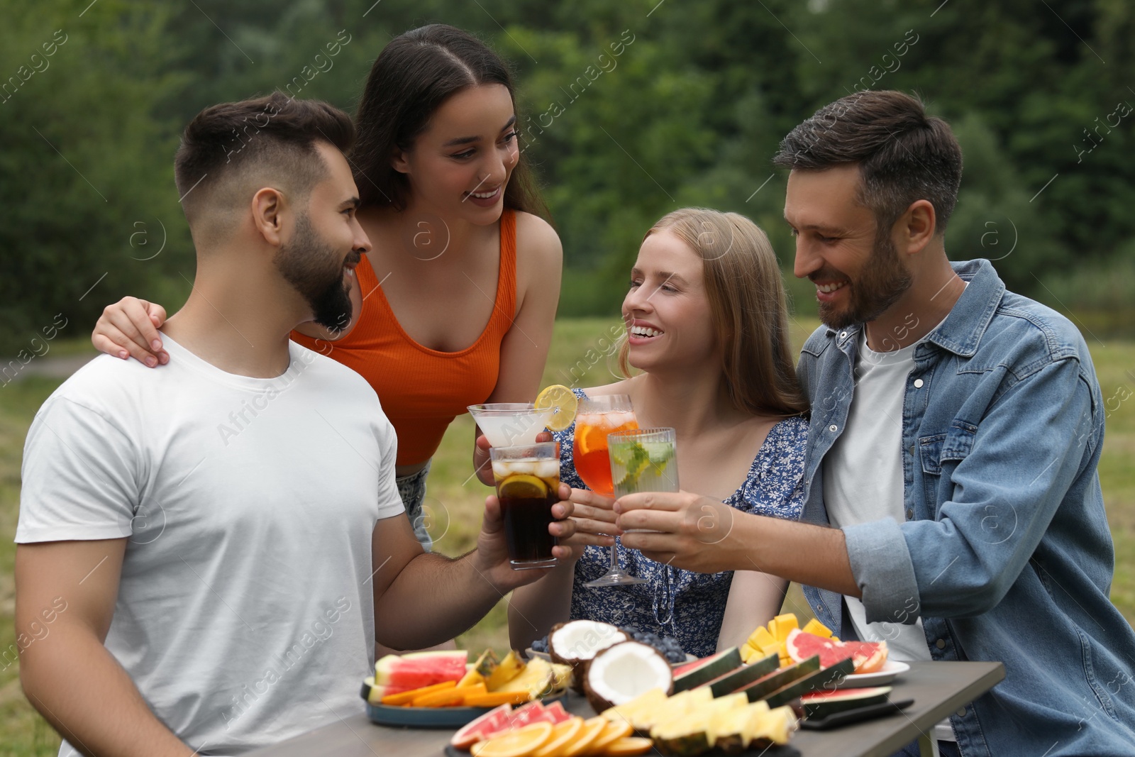 Photo of Happy friends clinking glasses with cocktails at table outdoors