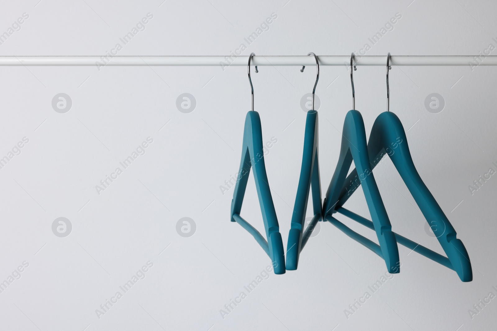 Photo of Blue clothes hangers on metal rail against light background. Space for text
