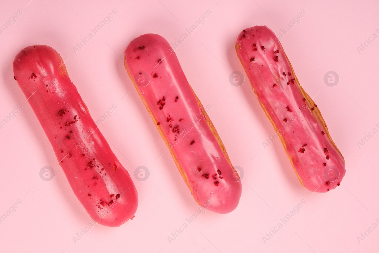 Photo of Delicious eclairs covered with glaze on pink background, top view