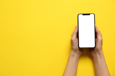 Woman with smartphone on yellow background, top view. Space for text