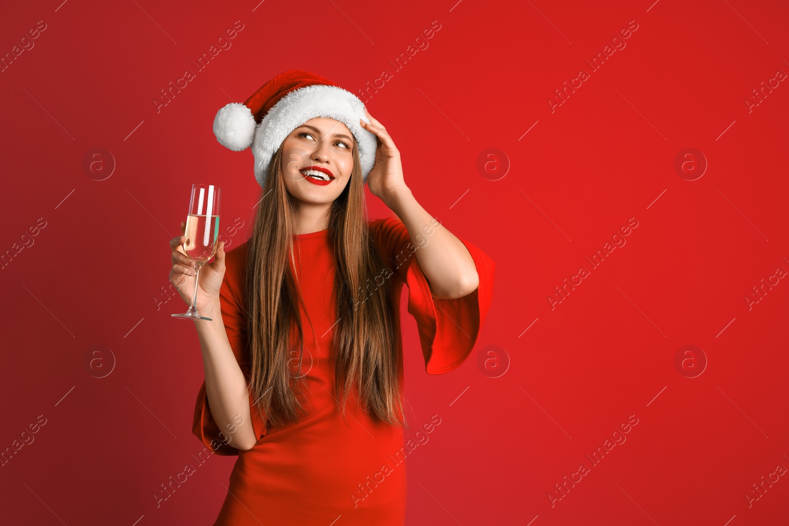 Photo of Young beautiful woman in Santa hat with glass of champagne on color background. Christmas celebration