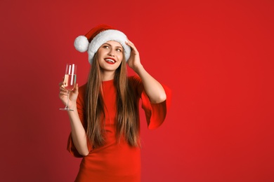 Photo of Young beautiful woman in Santa hat with glass of champagne on color background. Christmas celebration