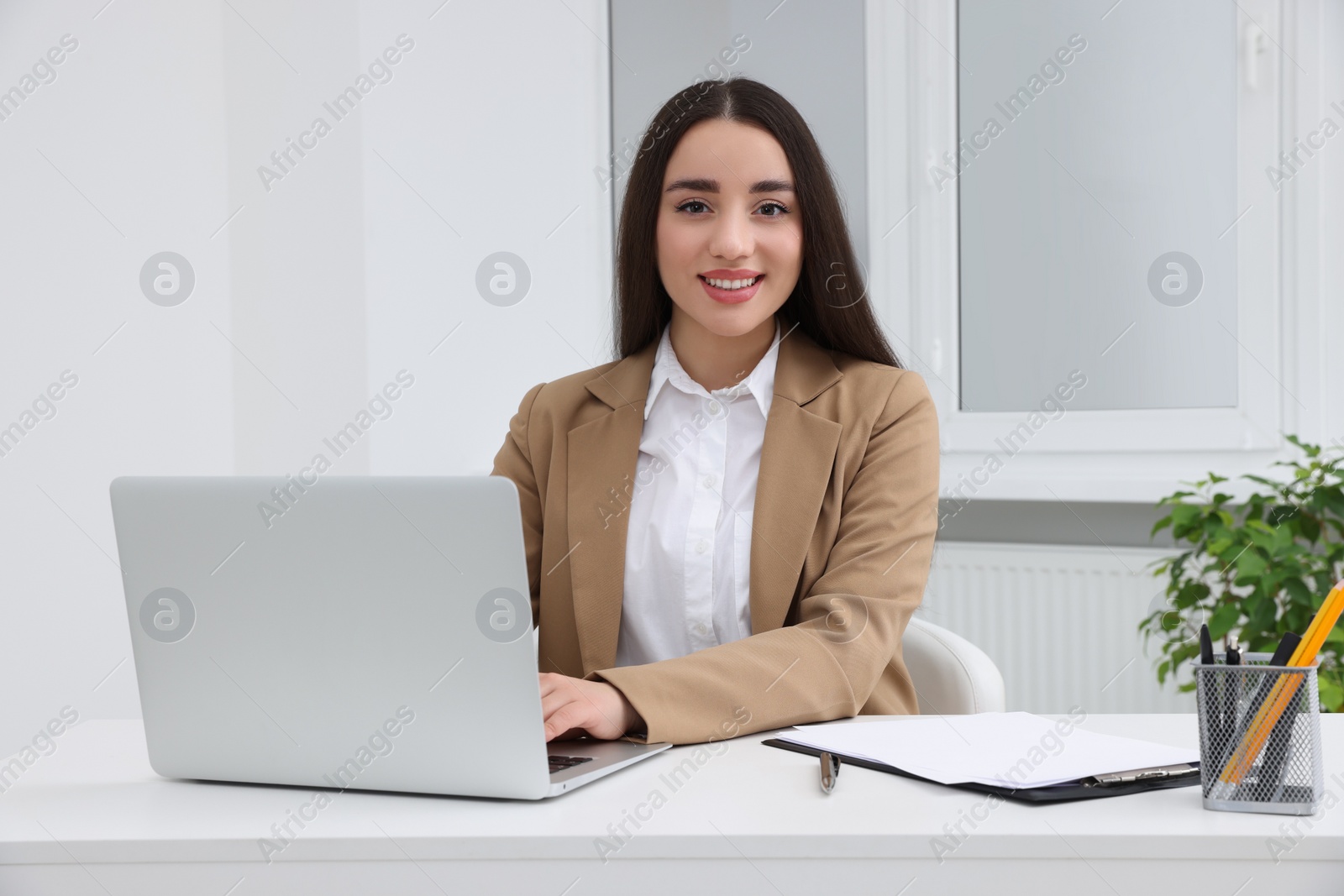 Photo of Young female intern working with laptop at table in office