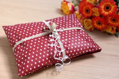 Photo of Parcel wrapped in heart patterned paper and beautiful flowers on wooden table, closeup