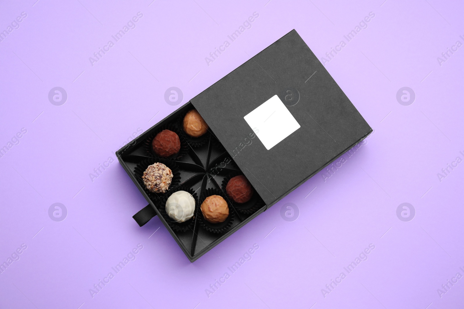 Photo of Box of tasty chocolate candies on violet background, top view