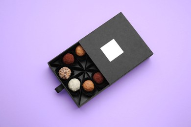 Photo of Box of tasty chocolate candies on violet background, top view
