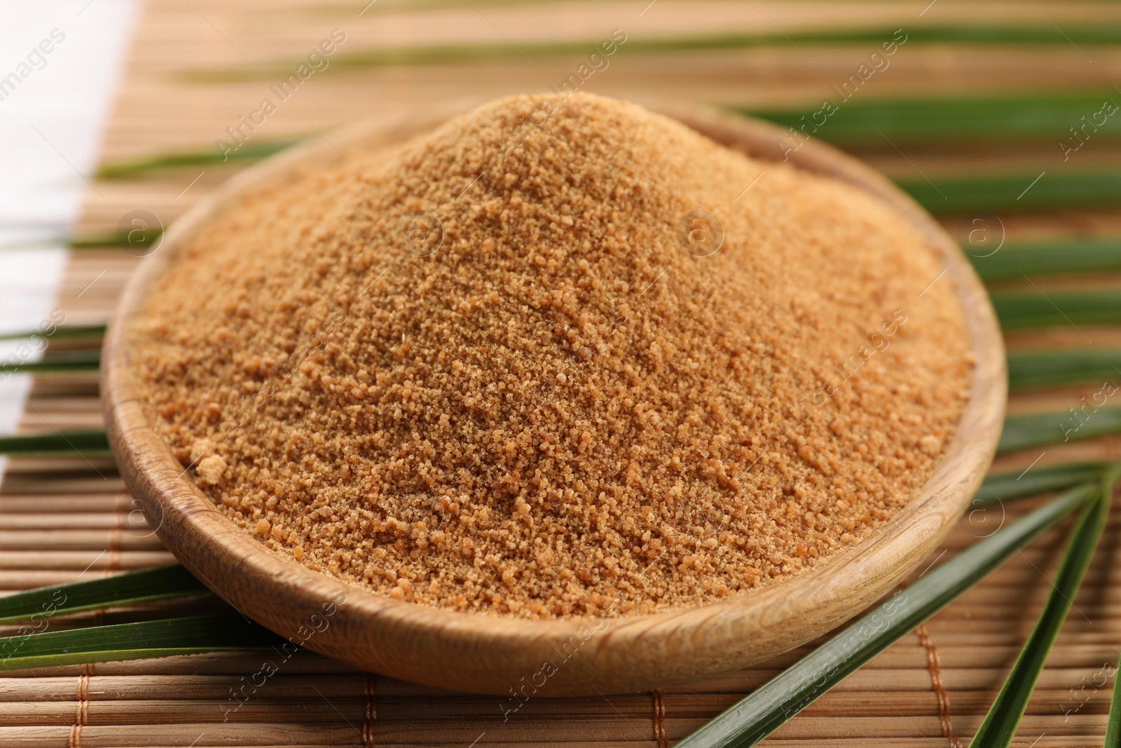 Photo of Coconut sugar, palm leaves and bamboo mat on table, closeup