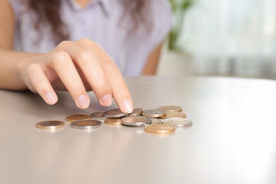 Young woman counting coins at table, closeup. Space for text