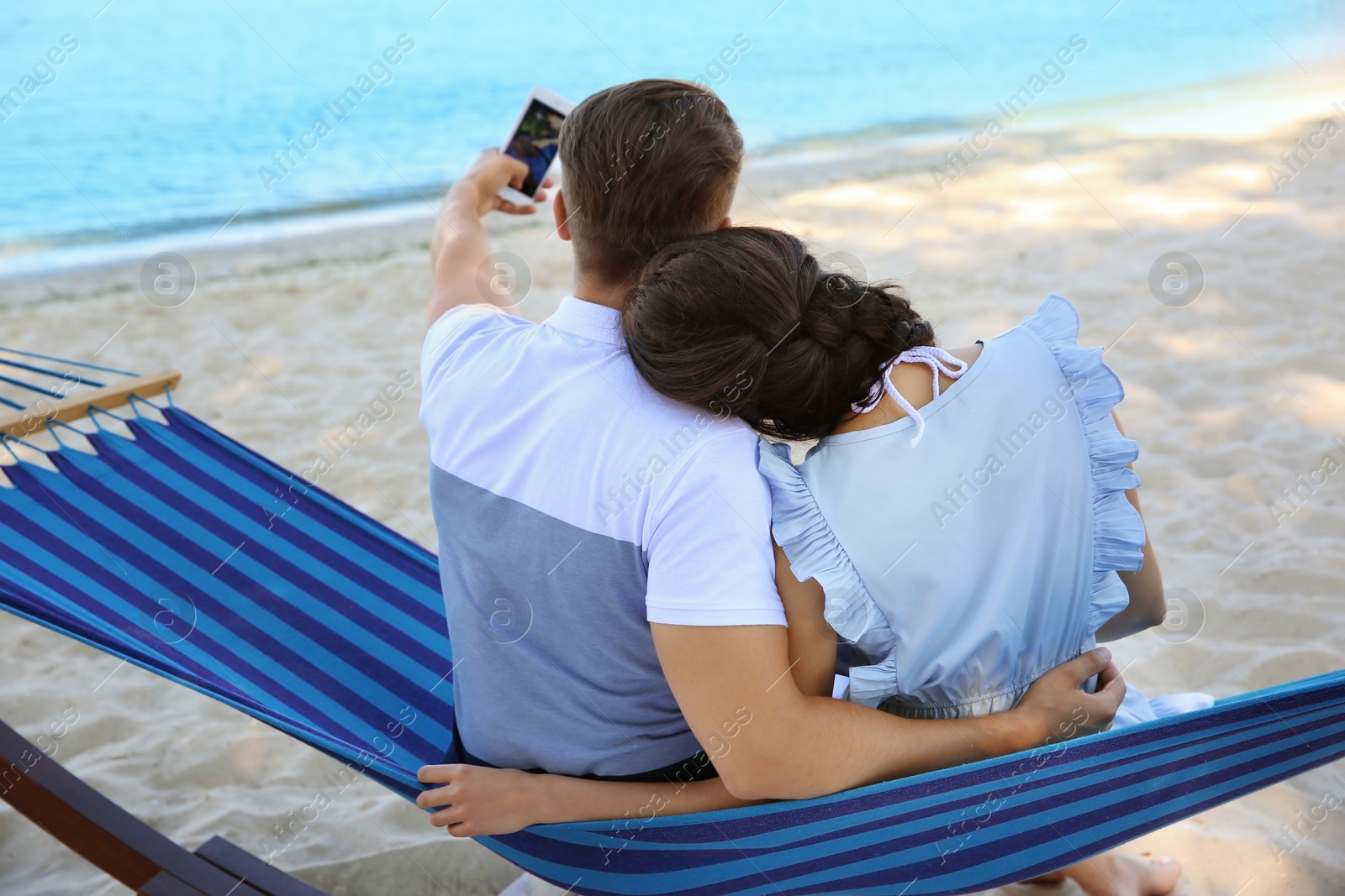 Photo of Young couple taking selfie in hammock at seaside