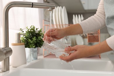 Woman washing glass at sink in kitchen, closeup