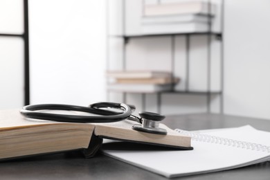 Photo of Open student textbook and stethoscope on grey table indoors. Medical education