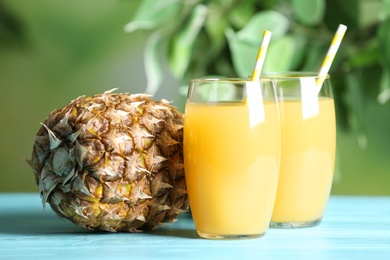 Photo of Freshly made pineapple juice in glasses on light blue table