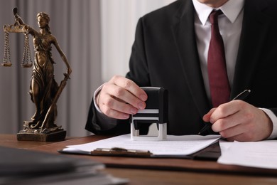 Notary with pen stamping document at wooden table in office, closeup