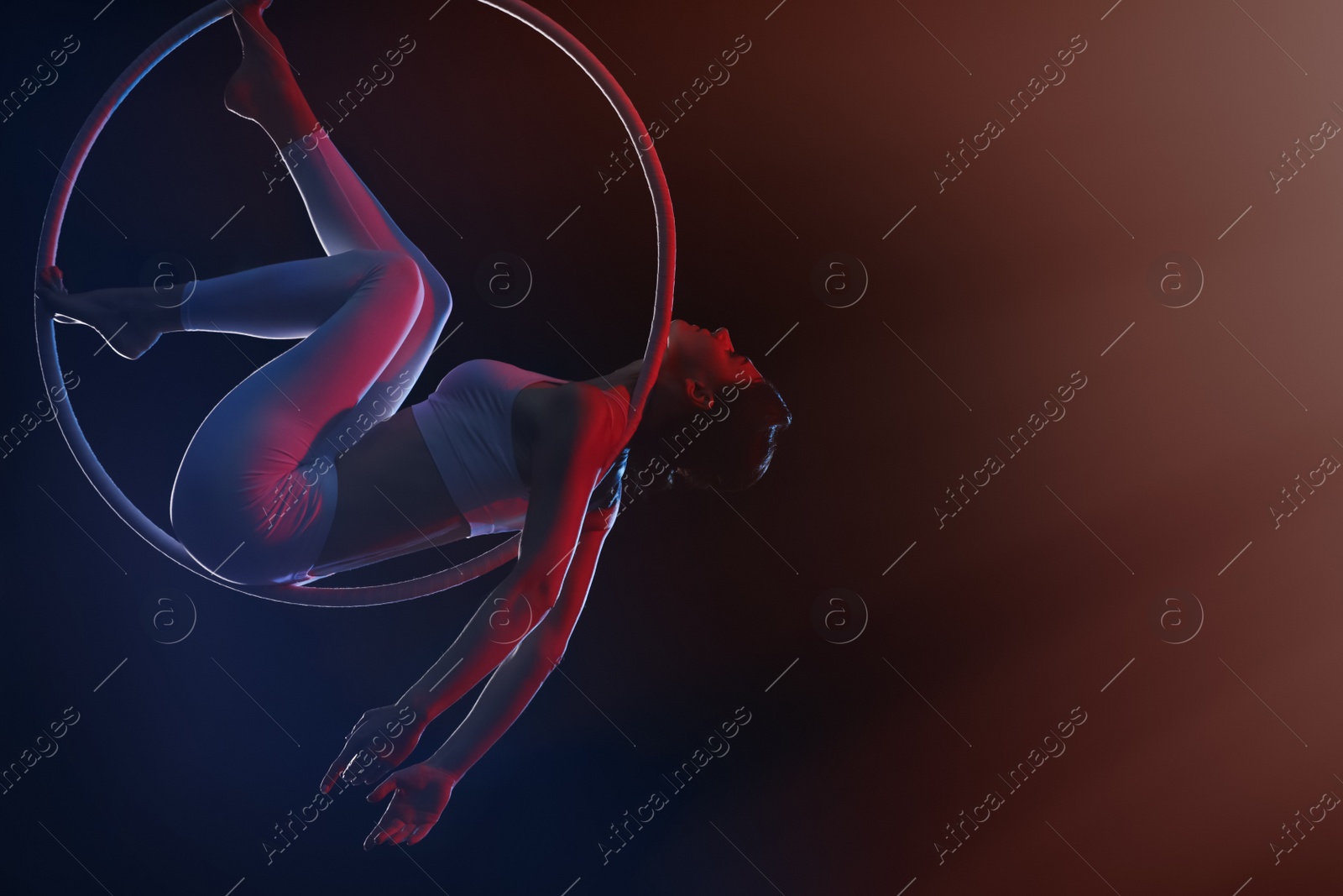 Photo of Young woman performing acrobatic element on aerial ring against dark background. Space for text