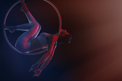 Young woman performing acrobatic element on aerial ring against dark background. Space for text