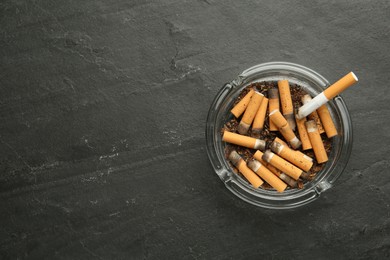 Photo of Glass ashtray with cigarette stubs on dark grey table, top view. Space for text