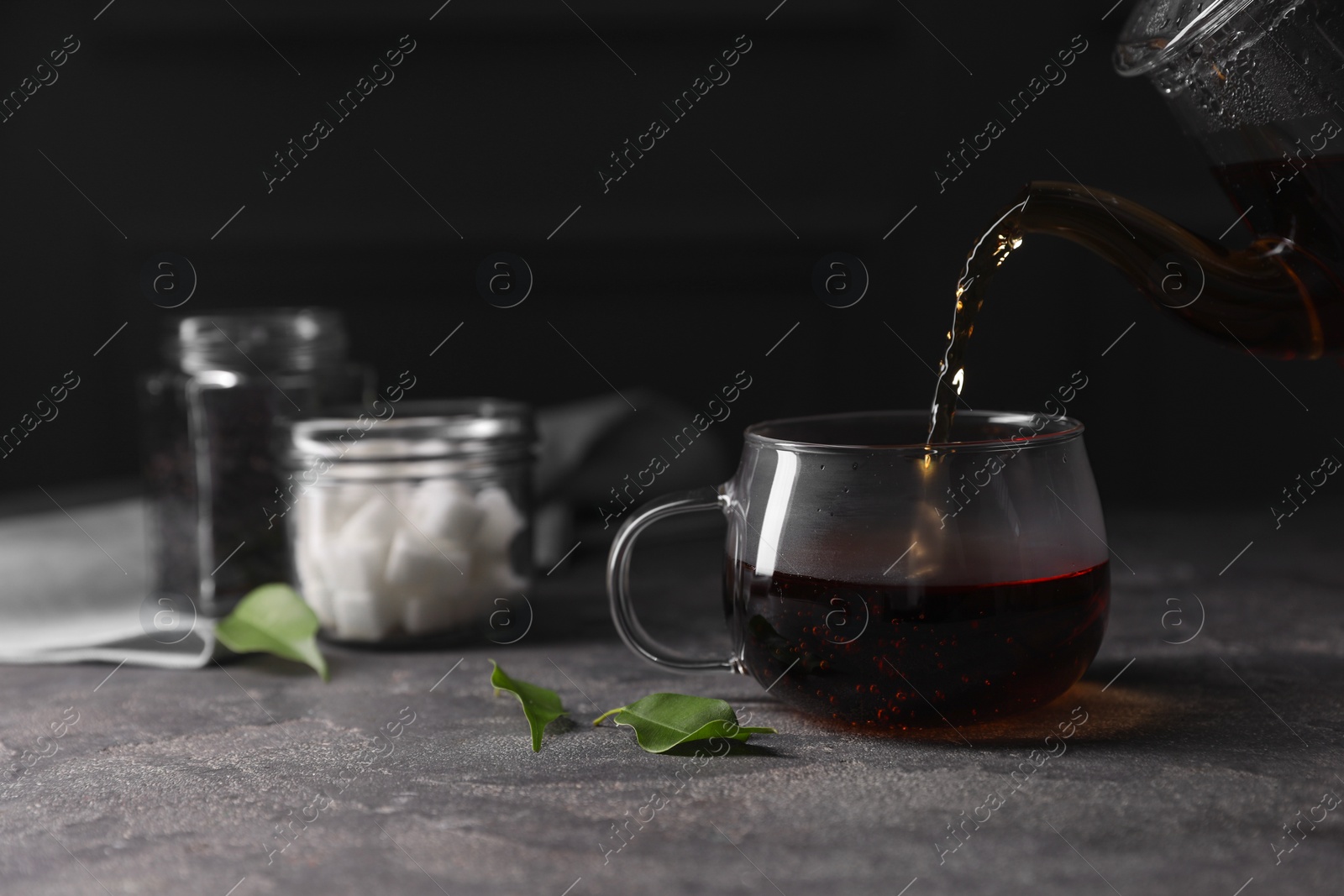 Photo of Pouring hot tea into cup on grey table, closeup