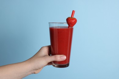 Photo of Woman holding glass with tasty smoothie, strawberry and straw on light blue background, closeup