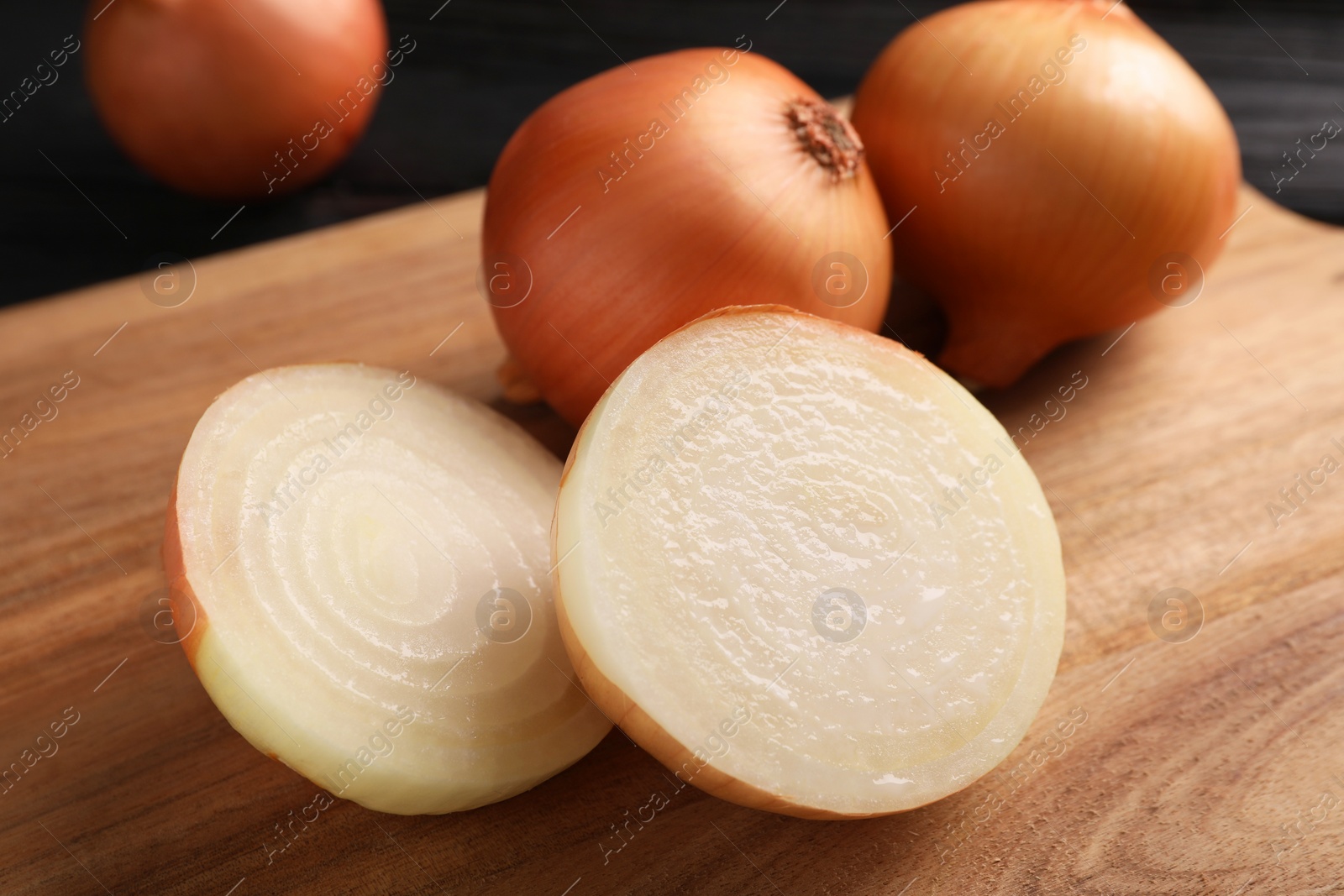 Photo of Whole and cut ripe onions on black wooden table, closeup