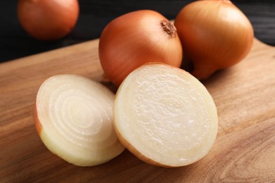 Photo of Whole and cut ripe onions on black wooden table, closeup