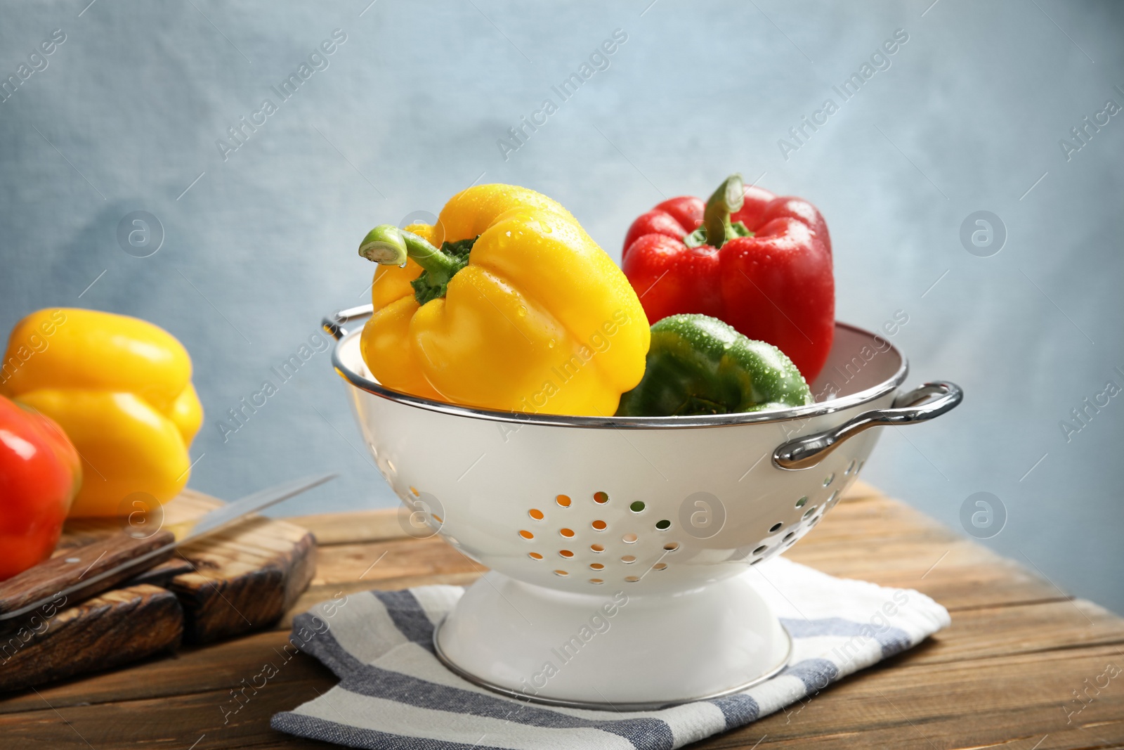 Photo of Colander with ripe paprika peppers on wooden table