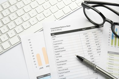 Accounting documents, pen, glasses and computer keyboard on white table, above view