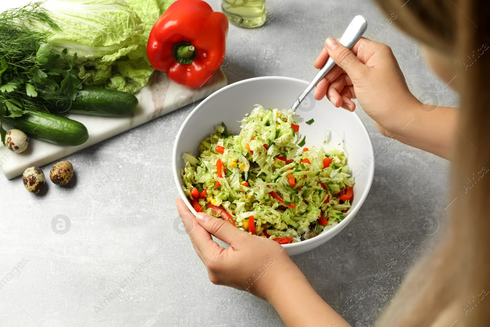 Photo of Woman making tasty salad with Chinese cabbage at light grey table, closeup