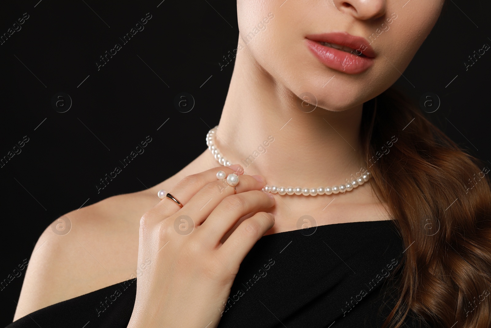 Photo of Young woman wearing elegant pearl jewelry on black background, closeup