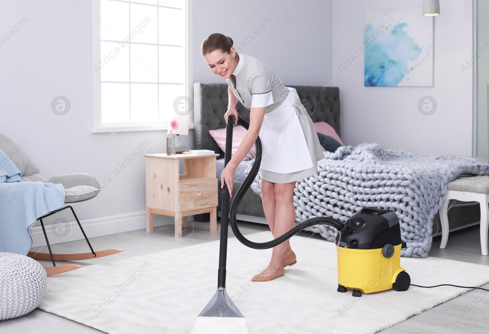 Photo of Young woman hoovering carpet with vacuum cleaner in bedroom