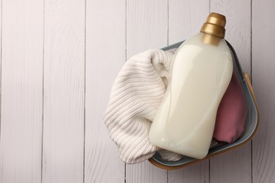 Photo of Bottle of fabric softener and clothes in basket on white wooden surface, top view. Space for text