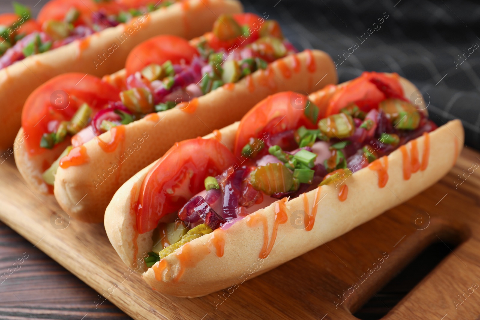 Photo of Tasty hot dogs with green onion, tomato, pickles and sauce on wooden table, closeup