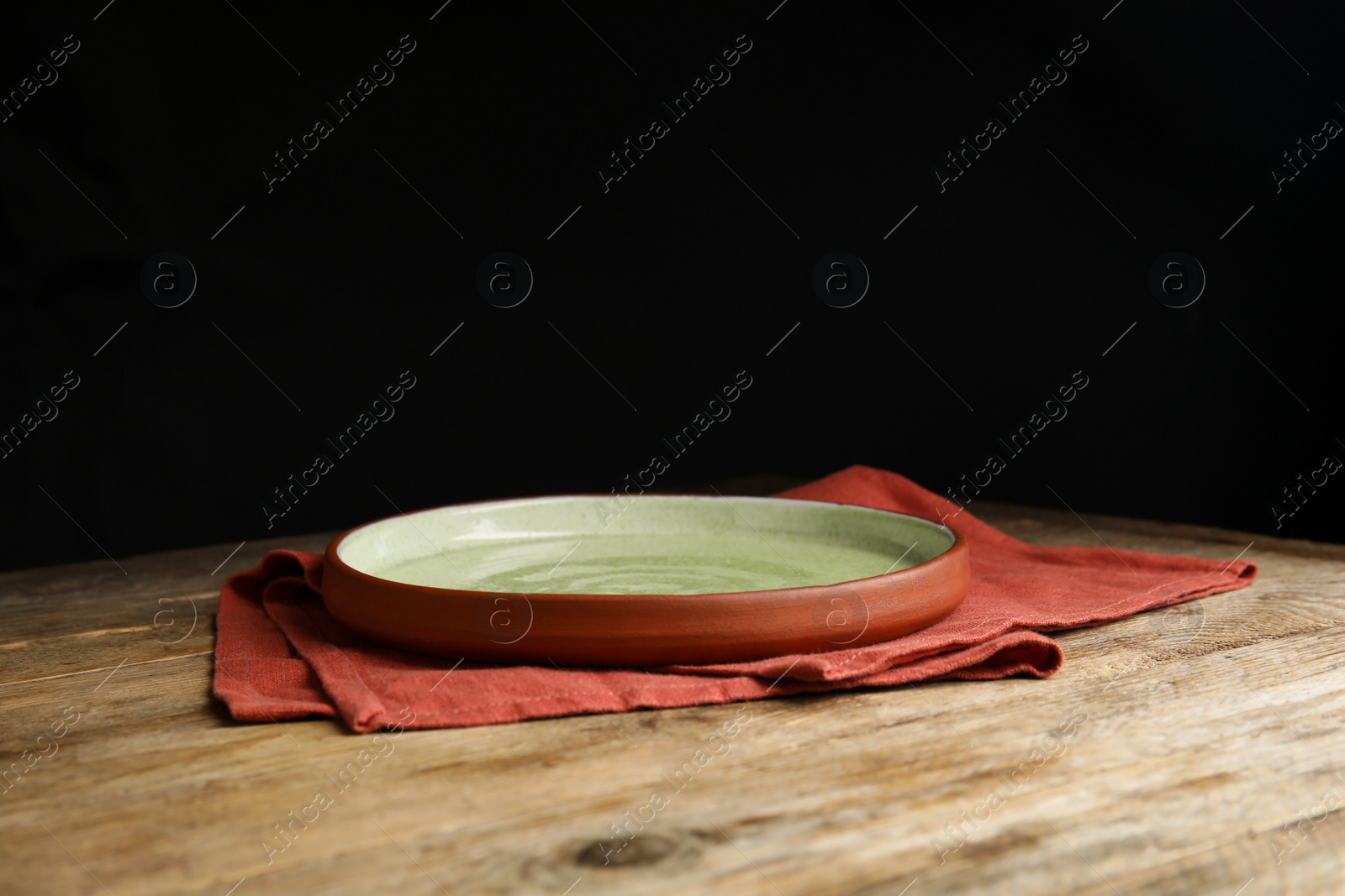 Photo of Empty plate and napkin on wooden table against black background