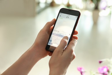 Woman writing message with text I Love You on smartphone against blurred background, closeup
