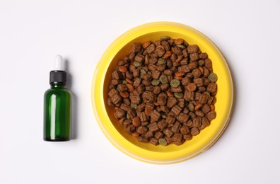 Photo of Glass bottle of tincture near dry pet food in bowl on white background, top view