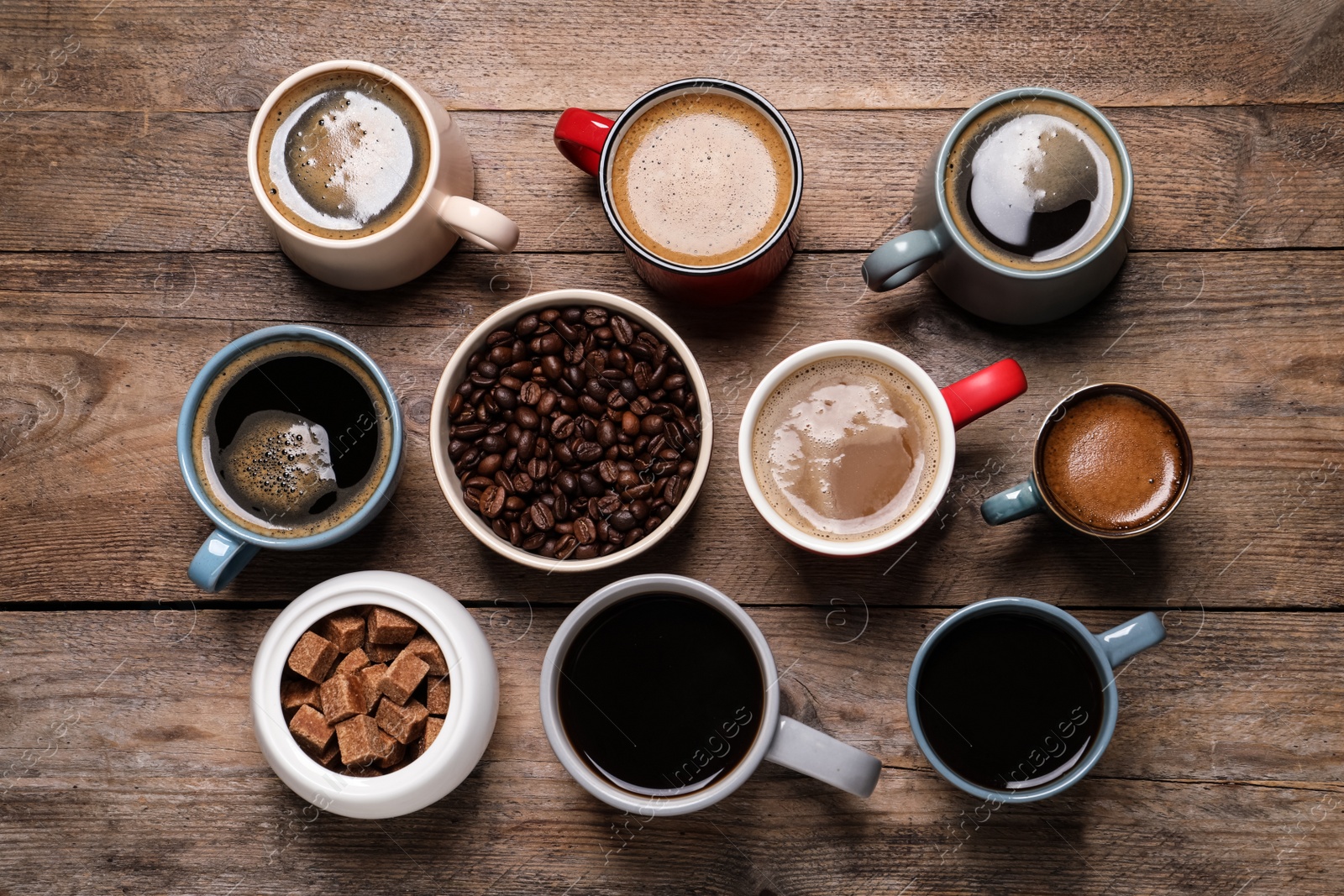 Photo of Cups of hot coffee with beans and sugar on wooden table, flat lay