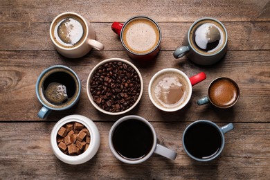 Photo of Cups of hot coffee with beans and sugar on wooden table, flat lay