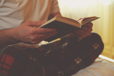 Photo of Young man reading book on bed at home, closeup