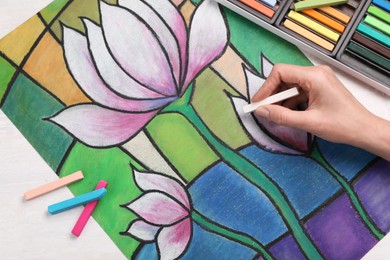 Woman drawing beautiful lotus flowers on paper with soft pastels at white table, top view