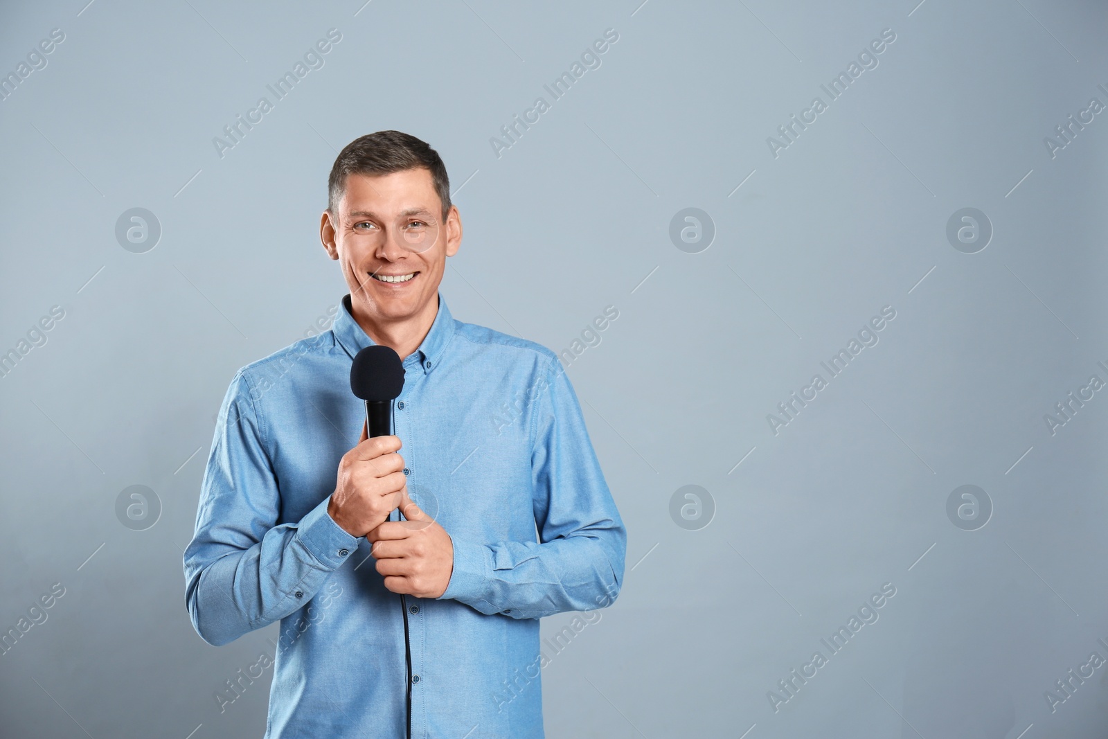 Photo of Male journalist with microphone on grey background. Space for text