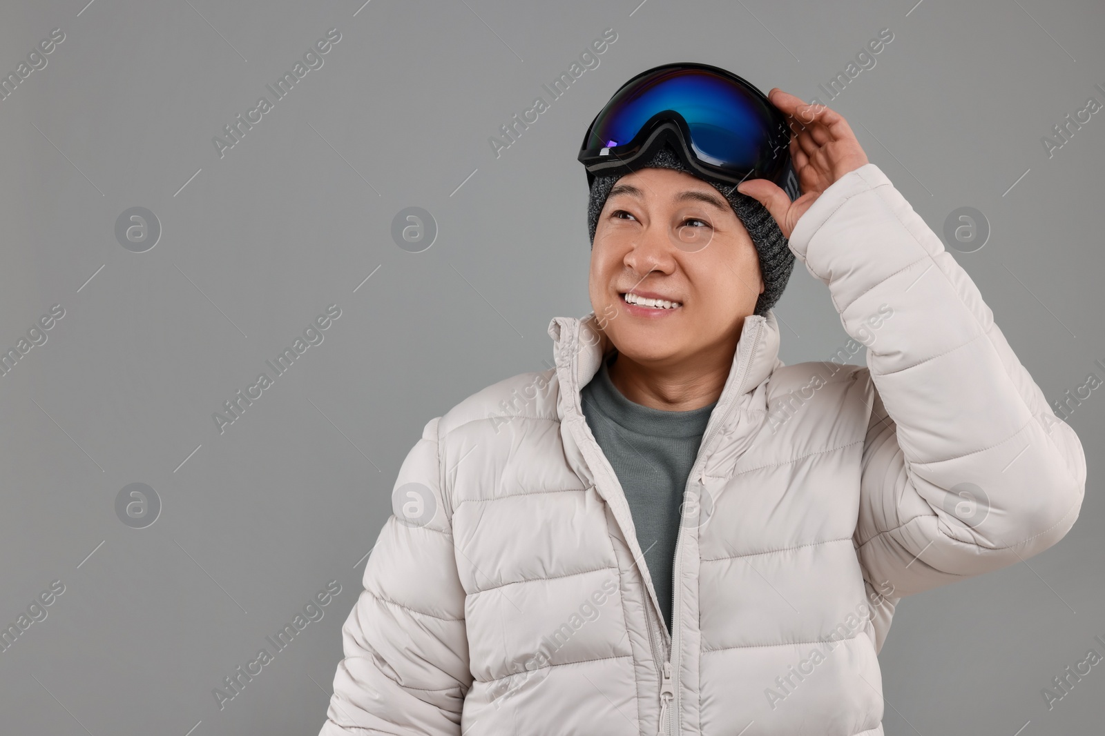 Photo of Winter sports. Happy man with ski goggles on grey background, space for text