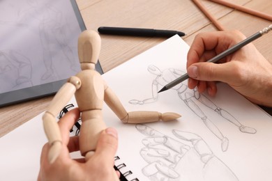 Photo of Man drawing mannequin in sketchbook with pencil at wooden table, closeup