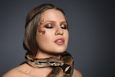 Beautiful woman with boa constrictor on grey background
