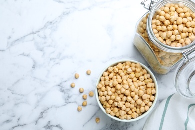 Photo of Bowl and jar with chickpeas on white marble table, flat lay. Space for text