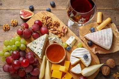 Photo of Flat lay composition with board of delicious cheese and snacks on wooden background