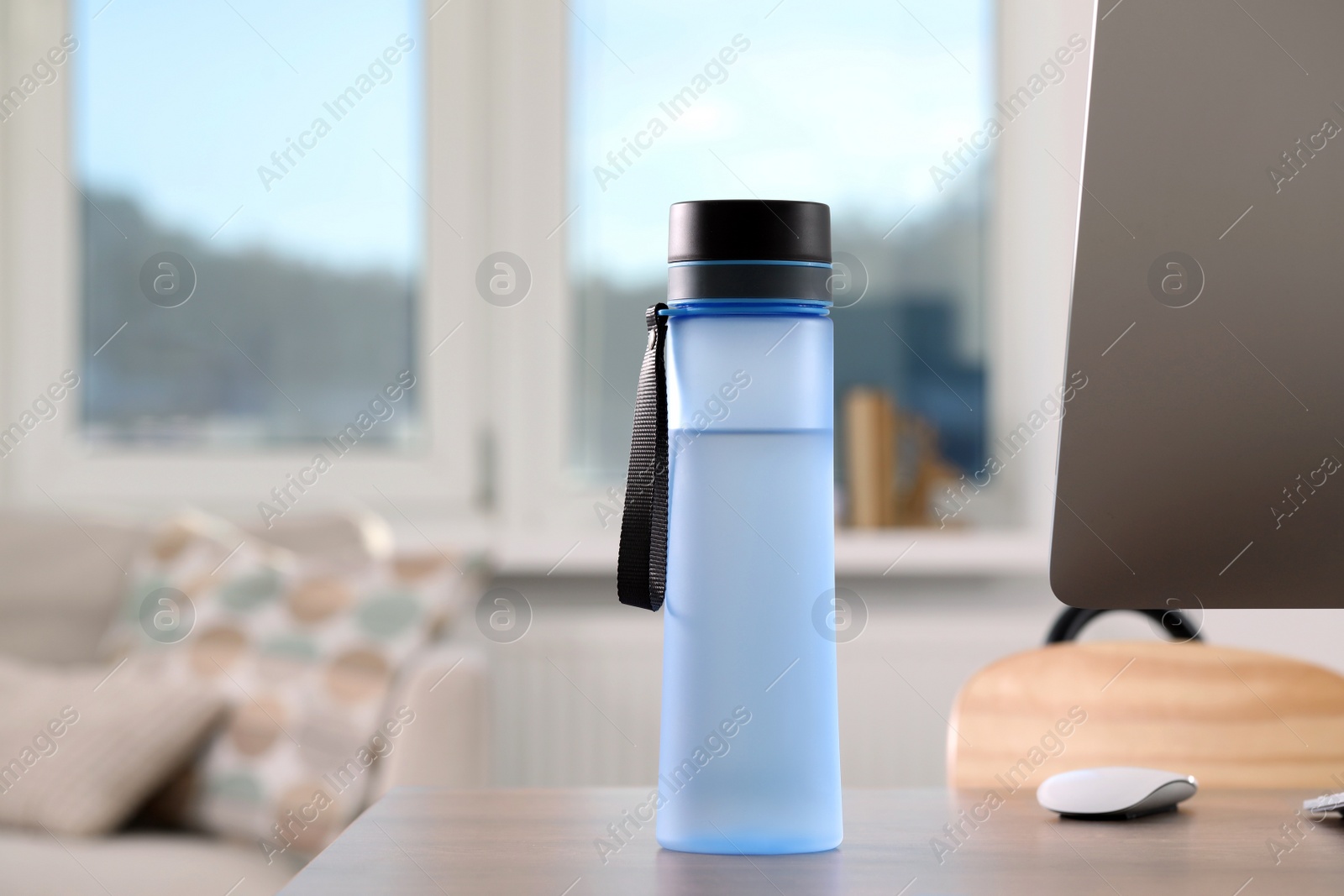 Photo of Stylish bottle of water and computer on table at workplace in office