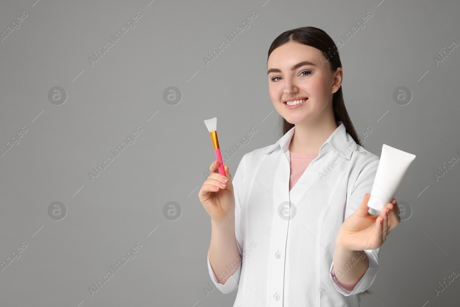 Photo of Cosmetologist with cosmetic product and silicone brush on grey background, space for text